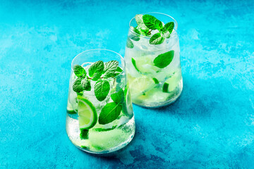 Lime lemonade, or limeade, in glasses with lime, mint, and ice. Fresh summer Mojito mocktail or cocktail, on a vibrant blue background