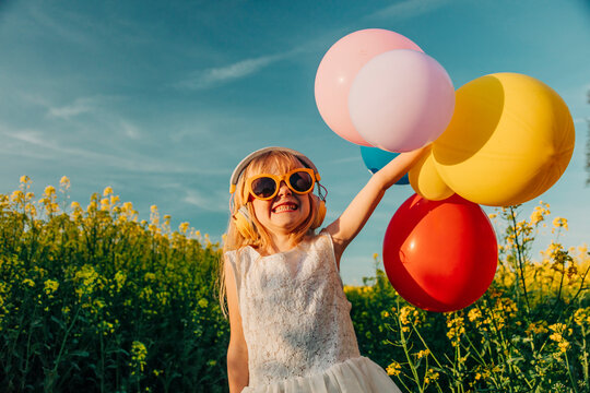 Girl in a white dress holding colorful balloons in a rapeseed field on a sunny day