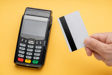 A person is holding a credit card in front of a payment terminal. The terminal has a green, yellow, and red button