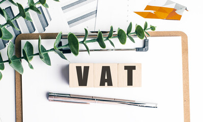 VAT acronym on wooden blocks with financial documents, clipboard, pen and eucalyptus leaves