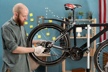 Bearded cyclist fixing bicycle wheel with wrench repairing and servicing bicycle at home DIY.