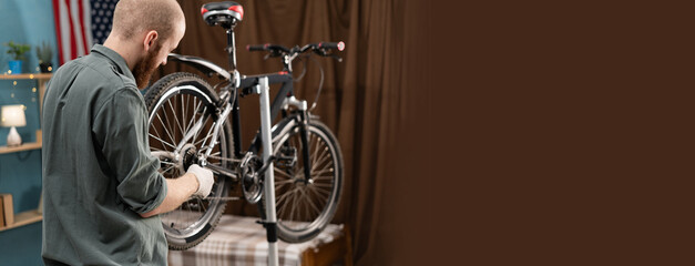 Bearded cyclist repairing bicycle at home, tightening nuts on wheel using wrench. Concept of indoor...
