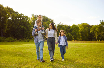 Smiling young happy family of four with two children boy and girl walking in the field together....