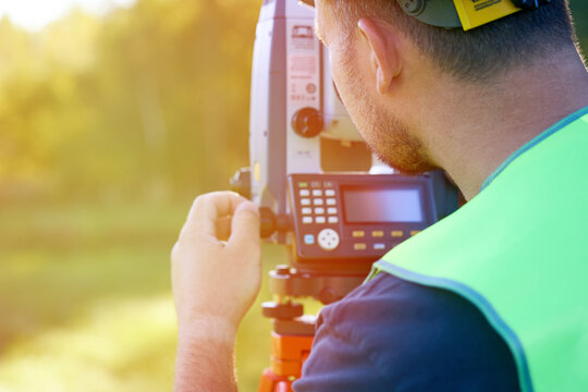 Engineer of surveyor protective vest and construction helmet near geodetic tool looks into distance. Implementation of geodetic tasks in land surveying and cadastral work