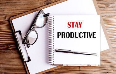 Stay productive phrase on spiral notebook with pen, clipboard and glasses on wooden desk