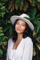 Beautiful Woman in White Hat Posing Gracefully Against Lush Greenery