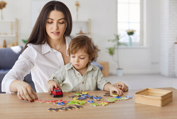 Mother and son, nanny woman and child sitting at table, playing together, engaging with puzzle game...
