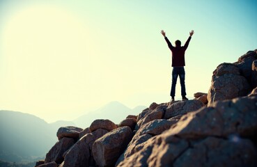 Obraz premium A person standing on rocky mountain terrain with arms raised in victory against a bright sky