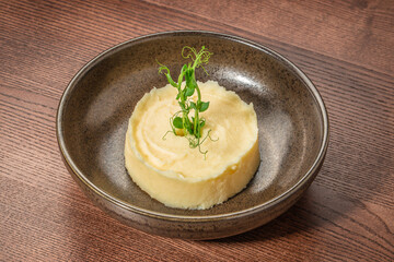 Creamy mashed potatoes elegantly plated with fresh pea shoots garnish on a rustic ceramic dish over wooden surface