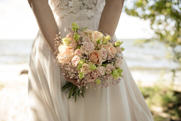 Braut hält romantischen Blumenstrauß am Strand – Sommerhochzeit in Pastellfarben
