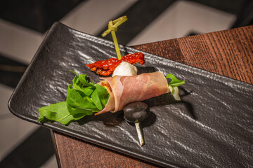 Elegant appetizer with prosciutto-wrapped arugula, mozzarella, sundried tomato, and black olive on...