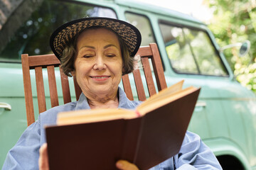 Enjoying a sunny afternoon in the garden, an elderly woman reads a book with joy and peace