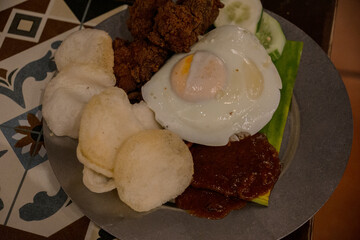Nasi Lemak with a fried egg with a slightly runny yolk, crispy fried chicken, cucumber slices,...