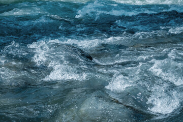 Dynamic shot capturing frothing movement of blue-tinged river water as it rushes over unseen obstacles. Untamed natural energy and motion.