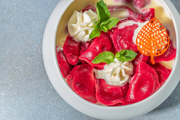 Bright red dumplings served with whipped cream, mint leaves, and white sauce in a modern white bowl