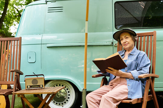Serene moments of a senior woman reading in a lush garden setting near a vintage van