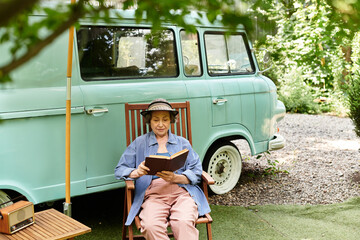 Enjoying a peaceful afternoon, a senior woman reads in her serene garden by a vintage van