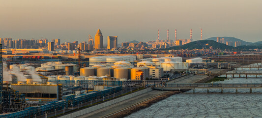 Large oil storage tanks and modern city skyline in industrial area at sunset