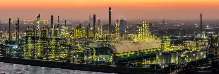 A large oil refinery and chemical plant brightly illuminated with steam rising from industrial equipment at dusk