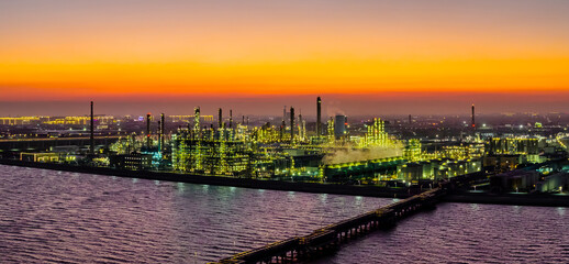 Aerial view of a large illuminated coastal oil refinery and chemical plant with industrial equipment at dusk