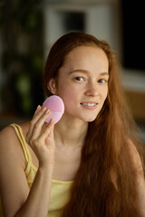 Beauty-tech. Portrait of cheerful woman with long hair using facial brush during skincare routine....
