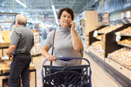 Elderly woman consulting on mobile phone while shopping at grocery store