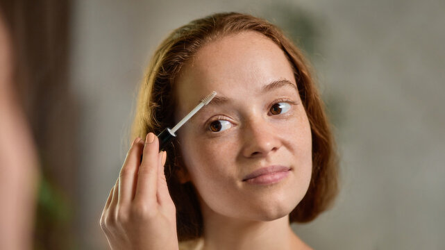 Clean-girl. Close-up portrait of calm woman brushing eyebrows with natural expression. Concept of self-care, makeup tutorials, minimalist cosmetics, natural beauty branding, morning routine. - Powered by Adobe
