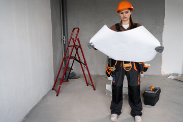 female builder reading blueprint before apartment renovation start