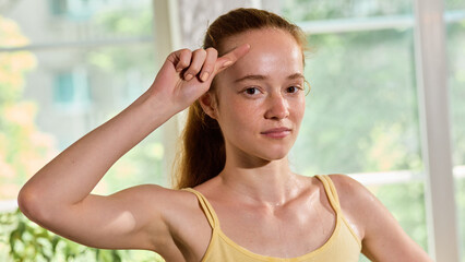Portrait of sweaty focused woman in yellow top raising hand after workout session. Concept of...