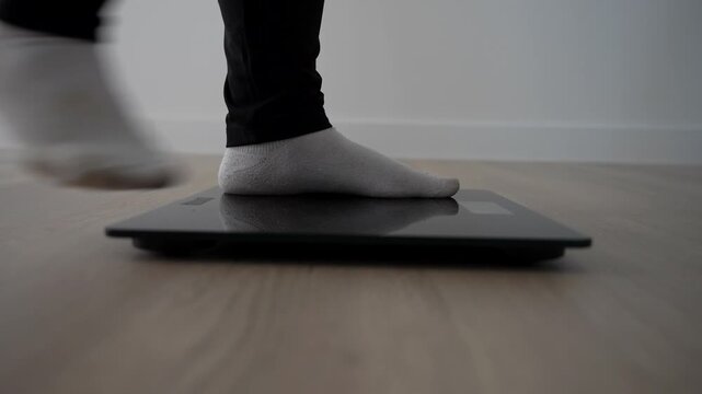 Profile shot of female feet stepping on digital scale to check weight on wooden floor