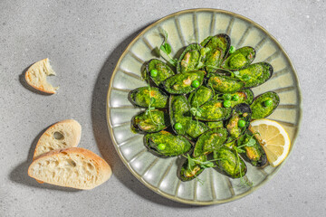 A plate of baked green mussels garnished with herbs and green peas is served with lemon wedges and...
