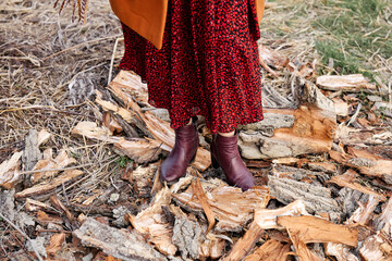 A close-up of boots and red skirt over scattered wood pieces in nature