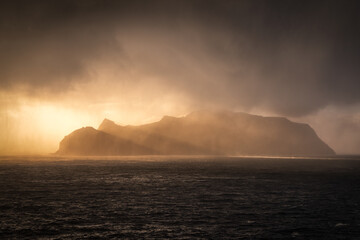 View of dramatic sunlight piercing through stormy clouds, illuminating the rugged coast and turbulent sea in the Faroe Islands, TÃ³rshavn, Faroe Islands.