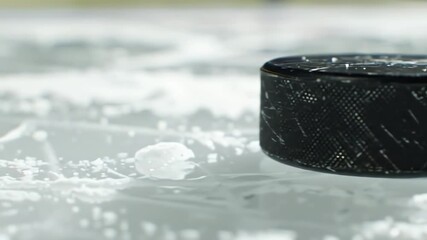 Cinematic slow motion close up of a hockey puck gliding across a frozen ice rink with ice shavings