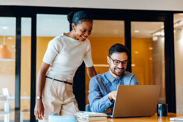 Smiling colleagues discussing ideas together at an office using a laptop