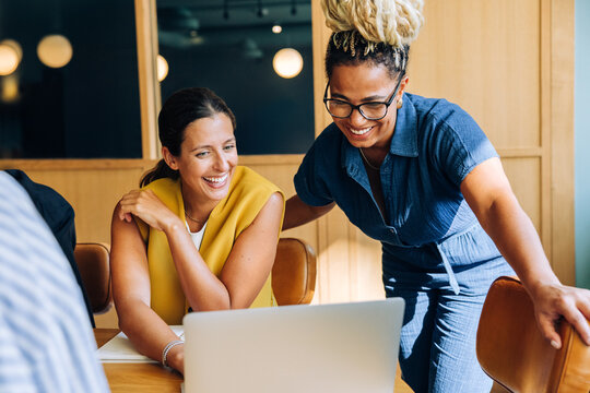 Two professional women smiling and working together at a desk with a laptop - Powered by Adobe