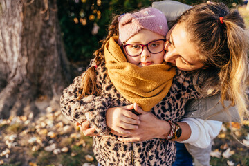 Mother embracing girl with Down syndrome in autumn park