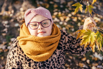 Girl with Down syndrome in glasses holding autumn leaves