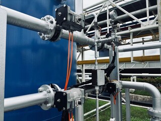 Modern industrial pipes and actuators with blue tank and orange wiring in factory setting,...