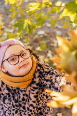 Portrait of girl with Down syndrome under autumn tree holding leaves