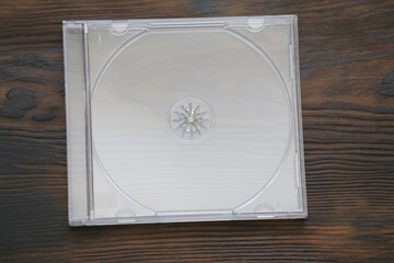  clear plastic CD jewel case, presented without artwork, sits on a textured, dark brown wooden surface