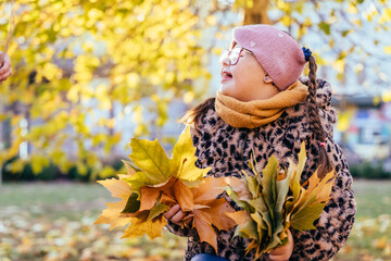 Girl with Down syndrome holding bunches of autumn leaves and smiling