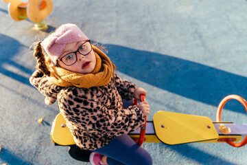 Girl with Down syndrome looking up from playground seesaw