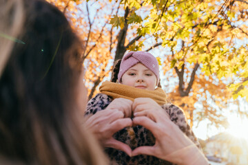 Girl with Down syndrome smiling behind heart hands