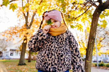 Girl with Down syndrome smiling and playing with green leaf in fall park