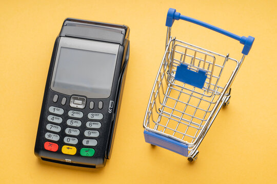 A shopping cart sits next to a payment terminal. The cart is empty and the terminal is black