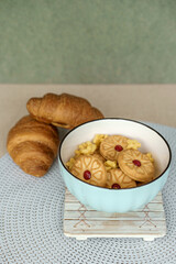 A sweet breakfast or snack in a blue bowl. Jam-filled cookies and star cereal with fresh croissants in the background. A cozy, delicious meal.