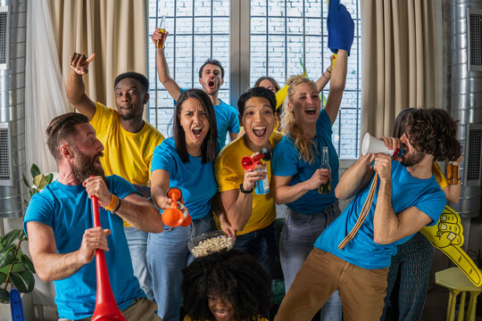 Excited multicultural group of young friends cheering loudly during a team match at home. Colorful energy, fun expressions, and vibrant team spirit fill the room. Celebration & diversity concept.