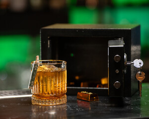 A sophisticated amber-colored cocktail, garnished with a rolled banknote, sits beside an open safe...