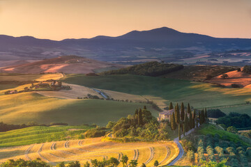 View of golden sunlight kissing the rolling hills and cypress trees leading to a Tuscan farmhouse, a serene landscape, San Quirico d'Orcia, Tuscany, Italy.